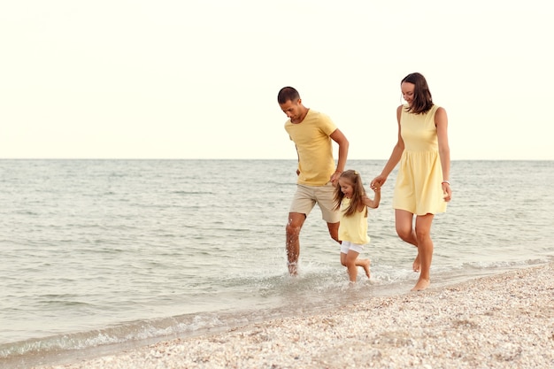 Jonge gelukkige familie in geel spel met hun kind aan zee