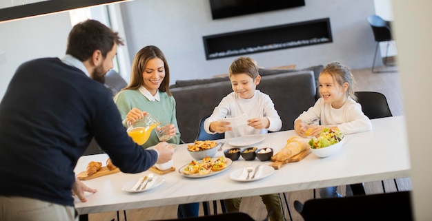 Jonge gelukkige familie praten tijdens het ontbijt aan de eettafel in het appartement