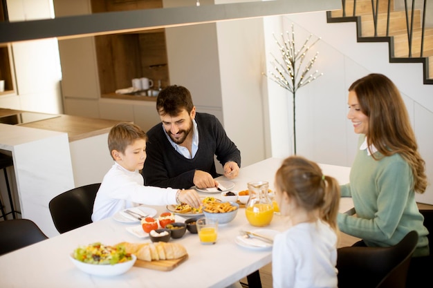 Jonge gelukkige familie praten tijdens het ontbijt aan de eettafel in het appartement