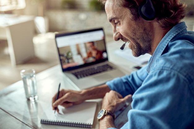 Foto jonge gelukkige freelance werknemer die aantekeningen maakt tijdens het werken op een laptop op kantoor