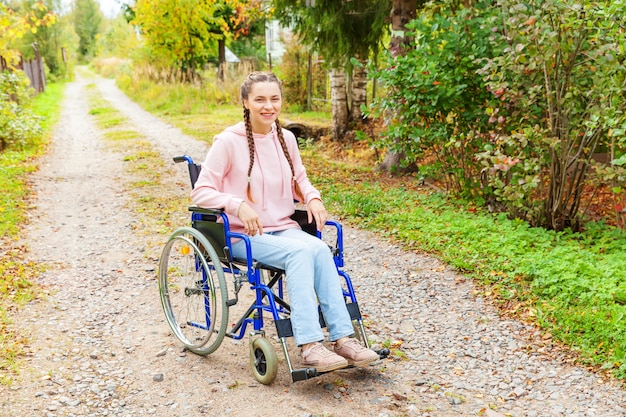 Jonge gelukkige handicapvrouw in rolstoel op weg in het ziekenhuispark die op de geduldige diensten wachten. Verlamd meisje in invalide stoel voor gehandicapten buiten in de natuur. Revalidatie concept.