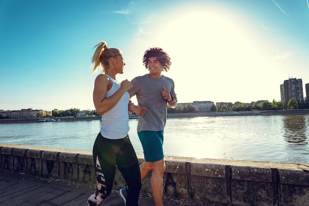 Jonge gelukkige hardlopers trainen buiten bij de rivier, trainen in de natuur tegen blauwe lucht met zonsopganglicht.