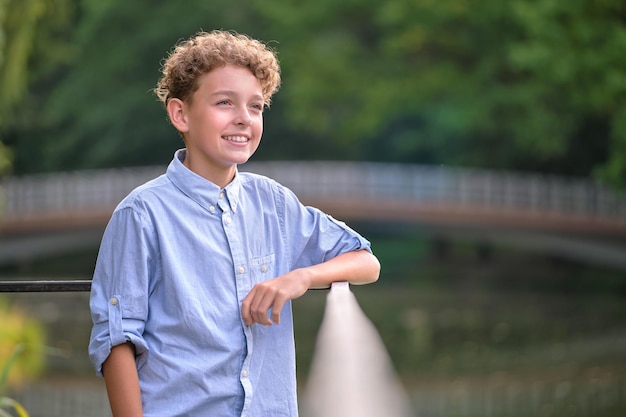 Jonge, gelukkige kindjongen die ontspant in het zomerpark Positief kind dat van de zomer in de buitenlucht geniet. Kinderwelzijnsconcept