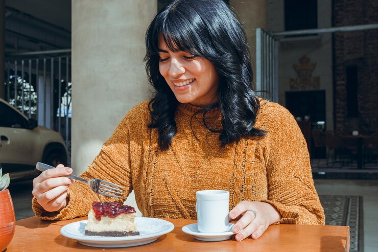 jonge gelukkige Latijnse vrouw die een plak cheesecake met vork snijdt