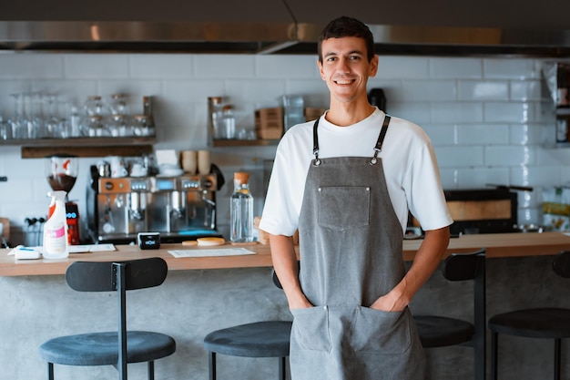 Jonge gelukkige man coffeeshop eigenaar of barista poseren met brede glimlach op het gezicht in café of koffiehuis