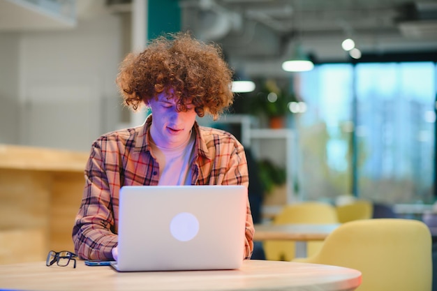 Jonge gelukkige mannelijke freelancer in vrijetijdskleding die in café met laptop zit en mobiele telefoon gebruikt