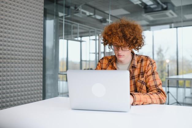 Jonge gelukkige mannelijke freelancer in vrijetijdskleding die in café met laptop zit en mobiele telefoon gebruikt