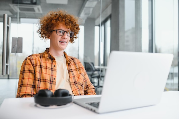 Jonge gelukkige mannelijke freelancer in vrijetijdskleding die in café met laptop zit en mobiele telefoon gebruikt