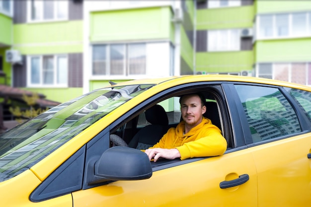 Jonge gelukkige mannelijke taxichauffeur zit achter het stuur van een taxi