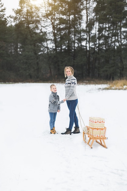 Jonge gelukkige moeder en haar zoon genieten van een slee rit in een prachtig besneeuwd winterbos