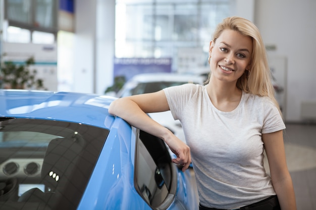 Jonge gelukkige mooie vrouw die na het kopen van nieuwe auto bij het handel drijven glimlachen