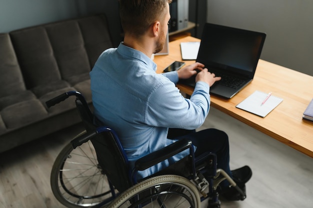 Jonge gelukkige ondernemer in rolstoel die aan laptop thuis werkt