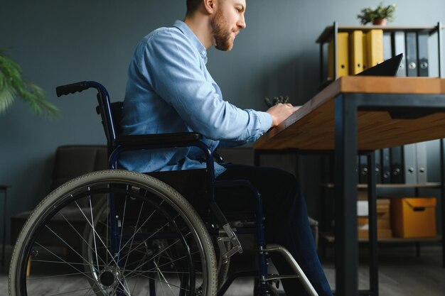 Jonge gelukkige ondernemer in rolstoel die aan laptop thuis werkt