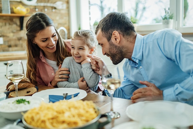 Jonge gelukkige ouders die plezier hebben met hun kleine dochter tijdens de lunch in de eetkamer