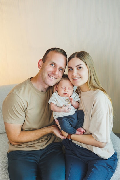 Jonge gelukkige ouders met een pasgeboren baby in hun armen thuis op de bank Moeder en vader met een nieuwgeboren baby op een witte achtergrond