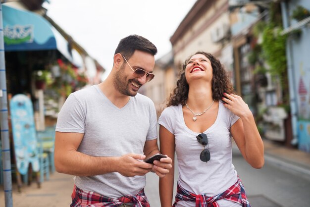 Jonge gelukkige paar met zonnebril wandelen door de stad en lachen.