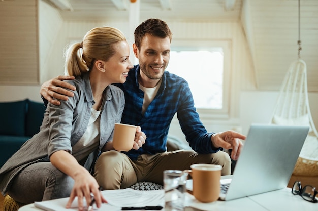 Jonge gelukkige paar praten terwijl ze koffie drinken en thuis op een computer werken