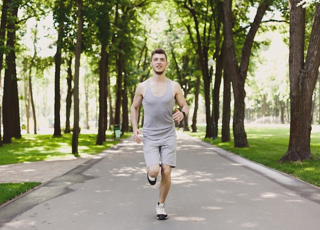 Jonge, gelukkige sportieve man die tijdens de ochtendtraining in het groene park loopt, kopieer ruimte