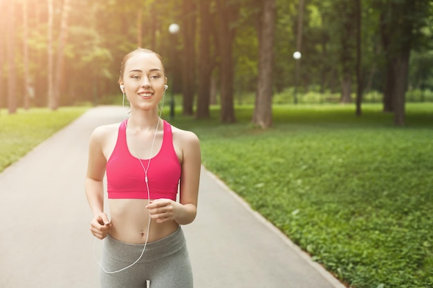 Jonge gelukkige sportieve vrouw die tijdens de ochtendtraining in het groene park loopt, kopieer ruimte