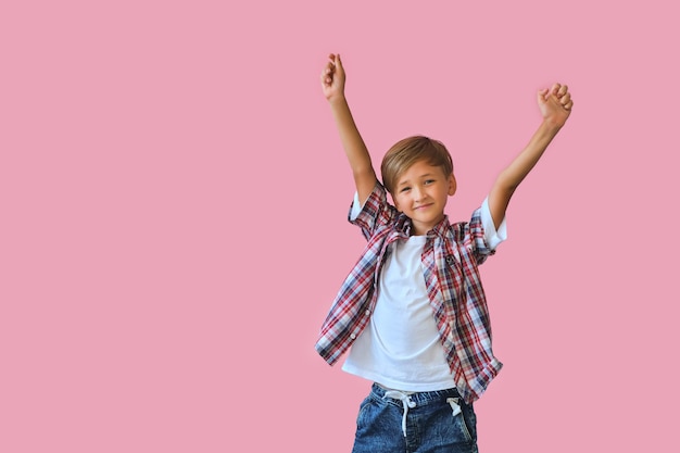 Jonge gelukkige tiener jongen met in casuals met opgeheven handen omhoog geïsoleerd op roze achtergrond.