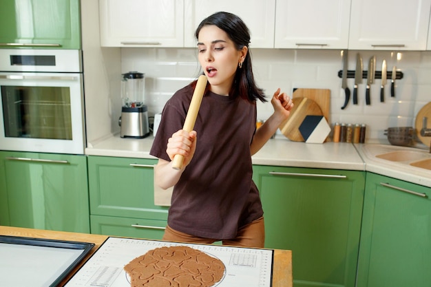 Jonge gelukkige vrolijke brunette gemengd ras vrouw zelfgemaakte koekjes bereiden tijdens het dansen