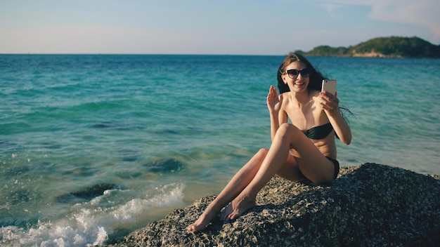 Jonge gelukkige vrouw chatten met vrienden via internet met behulp van smartphone in Ocean Beach