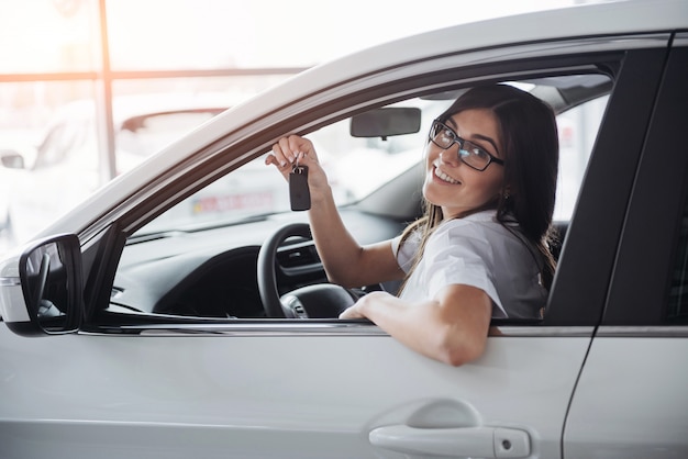 Jonge gelukkige vrouw dichtbij de auto met in hand sleutels