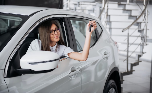 Jonge gelukkige vrouw dichtbij de auto met in hand sleutels