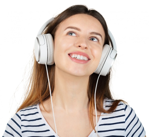 Jonge gelukkige vrouw die aan muziek met witte hoofdtelefoons luistert die op wit wordt geïsoleerd