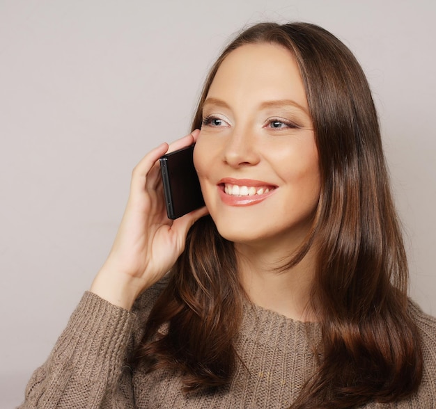 Jonge gelukkige vrouw die een mobiele telefoon gebruikt die op een witte achtergrond wordt geïsoleerd