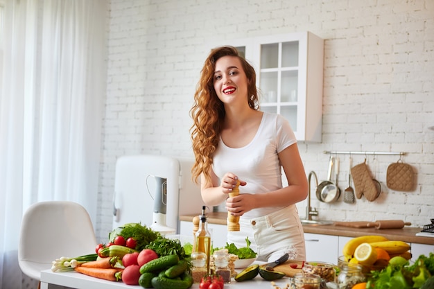 Jonge gelukkige vrouw die smakelijke salade in de mooie keuken met groene verse ingrediënten binnen voorbereiden. Gezond eten en dieet concept. Afvallen