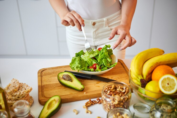 Jonge gelukkige vrouw die smakelijke salade in de mooie keuken met groene verse ingrediënten binnen voorbereiden. Gezond eten en dieet concept. Afvallen