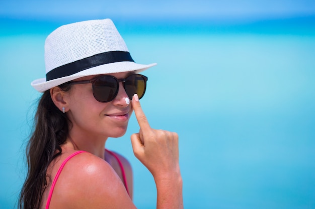 Jonge gelukkige vrouw die zonnebrandolie op haar neus op wit strand toepast