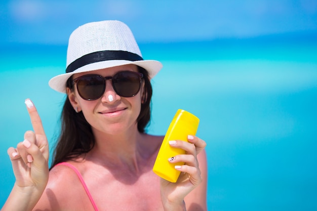 Jonge gelukkige vrouw die zonnebrandolie op haar neus op wit strand toepast