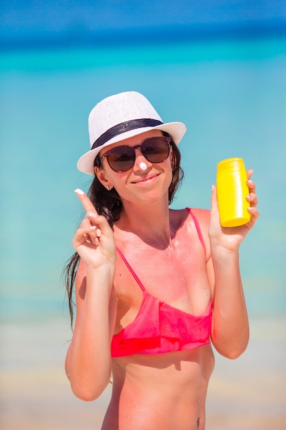 Jonge gelukkige vrouw die zonnebrandolie op haar neus op wit strand toepast