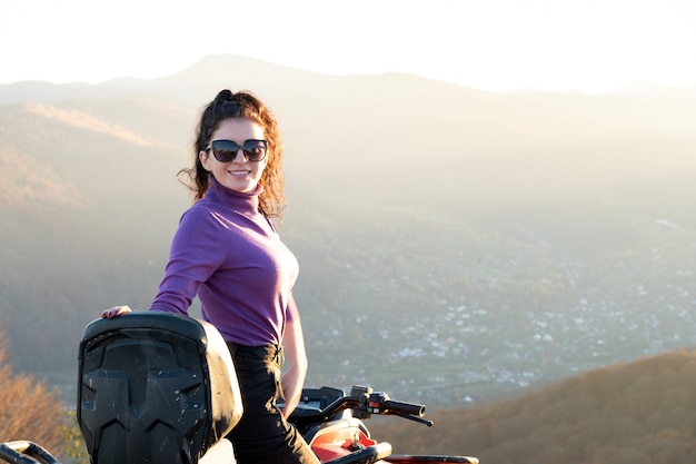 Jonge gelukkige vrouw genieten van extreme rit op atv quad motor in herfst bergen bij zonsondergang.