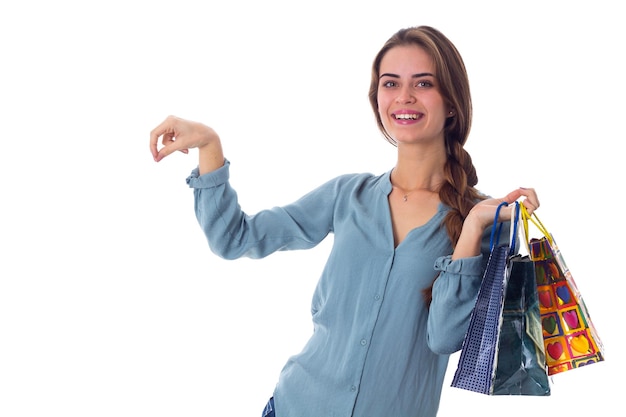 Jonge gelukkige vrouw in blauwe blouse met veelkleurige boodschappentassen en iets in haar hand