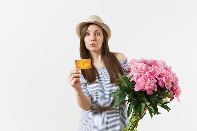 Jonge gelukkige vrouw in blauwe jurk, hoed met creditcard, geld, boeket van mooie roze pioenrozen bloemen geïsoleerd op een witte achtergrond. Zaken, levering, online winkelconcept. Ruimte kopiëren.