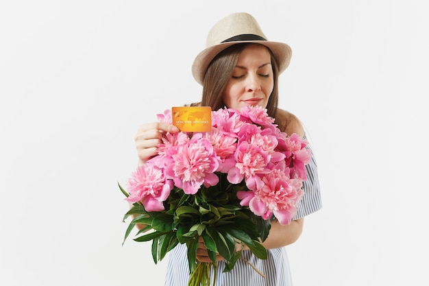 Jonge gelukkige vrouw in blauwe jurk, hoed met creditcard, geld, boeket van mooie roze pioenrozen bloemen geïsoleerd op een witte achtergrond. zaken, levering, online winkelconcept. ruimte kopiëren.