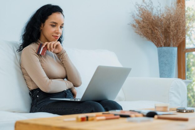 Jonge gelukkige vrouw koopt een product door thuis online te winkelen terwijl ze artikelen via internet bestelt met een online betalingssysteem met creditcard, beschermd door cruciale cyberbeveiliging van het online winkelplatform