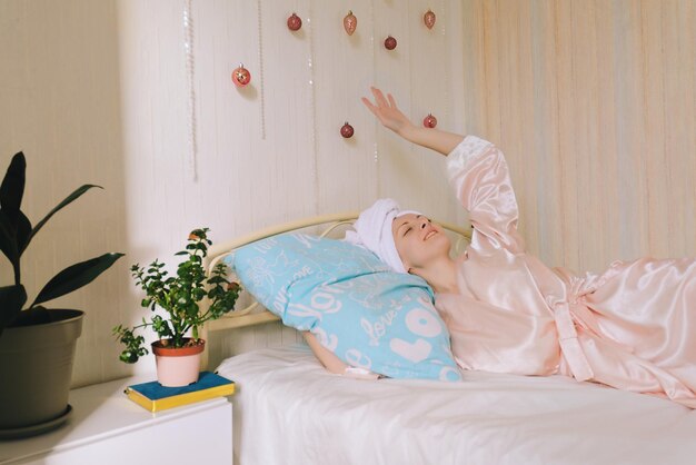 Jonge gelukkige vrouw met een handdoek op het hoofd ligt in bed in pyjama. gezellig huis. notitieboekje. Schoonheidsroutine