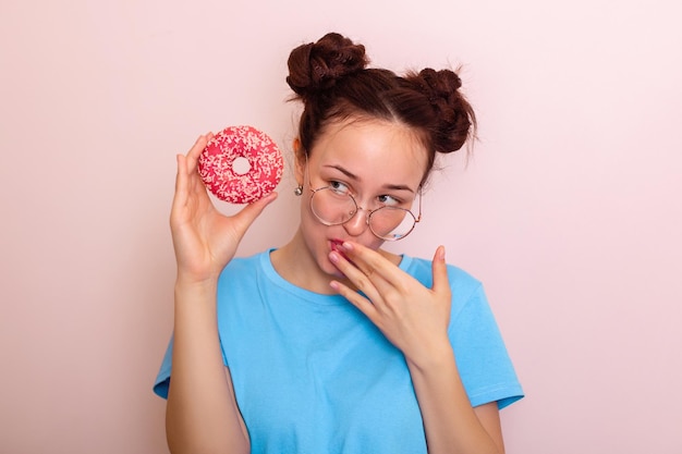 Jonge gelukkige vrouw met modekapsel die roze donut vasthoudt en glimlacht