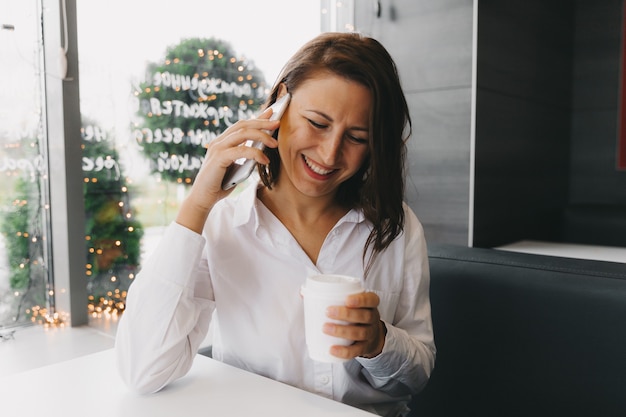 Jonge gelukkige vrouw praten op een mobiele telefoon in een coffeeshop, een dame met een mooie glimlach praten op een mobiele telefoon zittend in een café tijdens de lunch