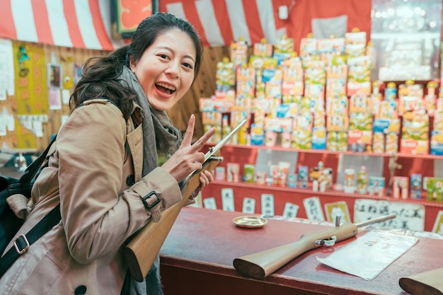 jonge gelukkige vrouw toeristische spelen schietspel op japanse tempel beurs in het voorjaar. overwinning vrouwelijke overwinning en het tonen van v-teken gezicht camera glimlachen. vrolijke dame backpacker opgewonden in straatverkoper
