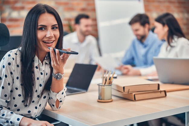 Jonge gelukkige vrouw zit aan het bureau terwijl haar collega in de moderne vergaderruimte werkt