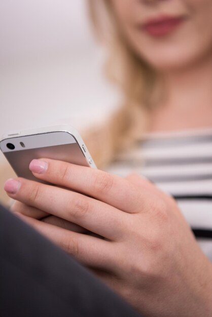 jonge gelukkige vrouw zittend op de Bank met mobiele telefoon bij luxe huis