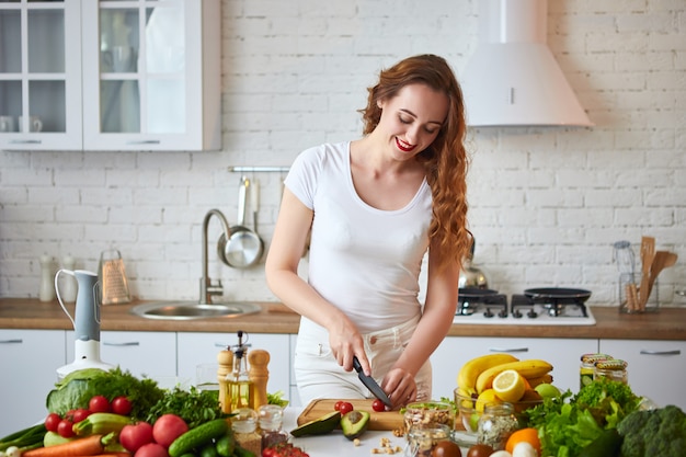 Jonge gelukkige vrouwen scherpe tomaten voor binnen het maken van salade in de mooie keuken met groene verse ingrediënten. Gezond eten en dieet concept. Afvallen
