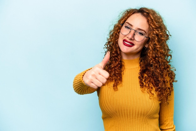 Jonge gember blanke vrouw geïsoleerd op blauwe achtergrond glimlachend en duim omhoog