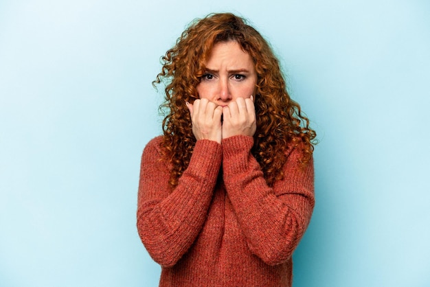 Foto jonge gember blanke vrouw geïsoleerd op blauwe achtergrond vingernagels bijten nerveus en erg angstig