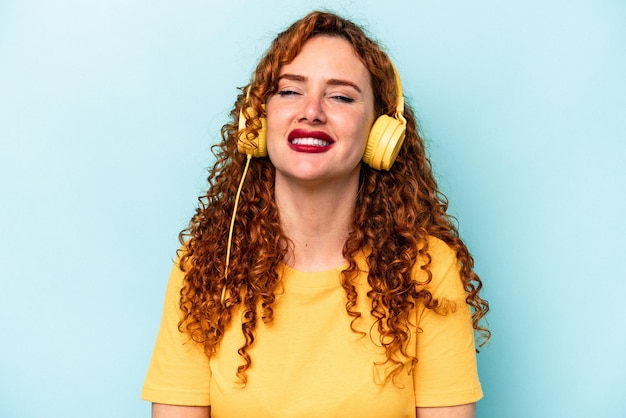 Jonge gember vrouw luisteren naar muziek geïsoleerd op blauwe achtergrond lachen en plezier